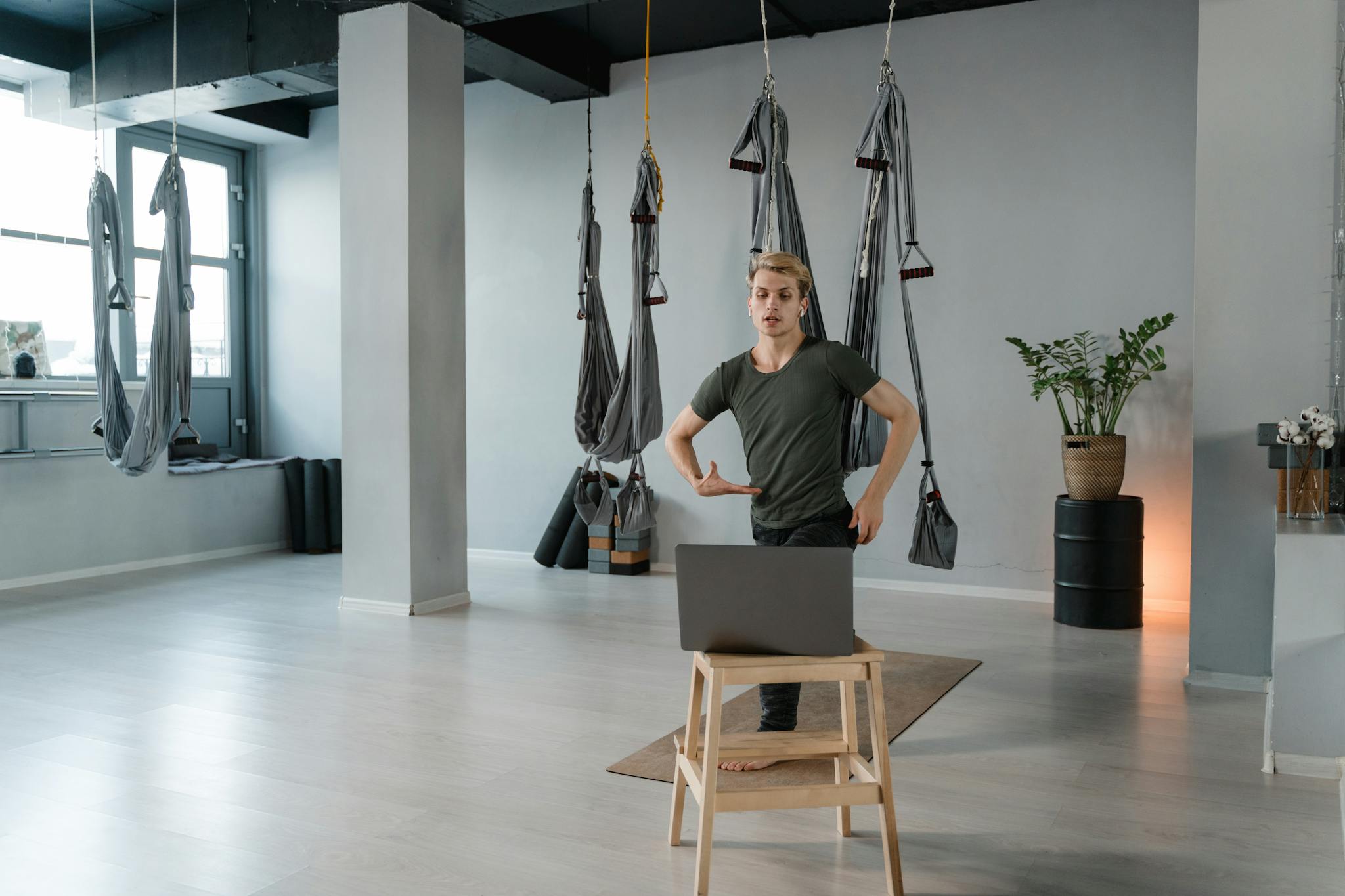 A man practicing aerial yoga in a contemporary studio setting using a laptop.