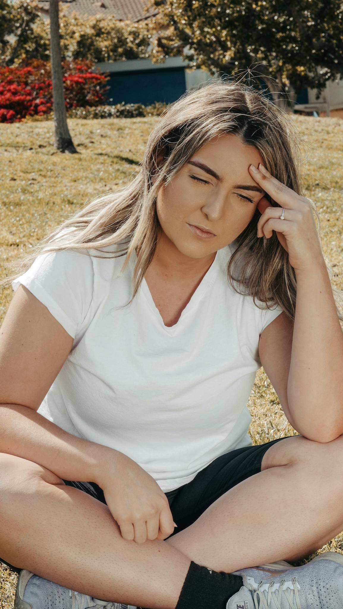 A woman sitting outdoors in a park, experiencing a headache, on a sunny day.