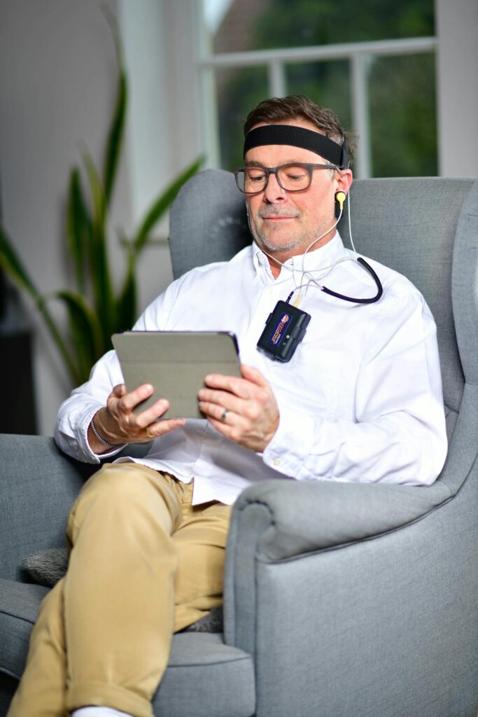 Man sitting in armchair using a neurofeedback device with tablet indoors.